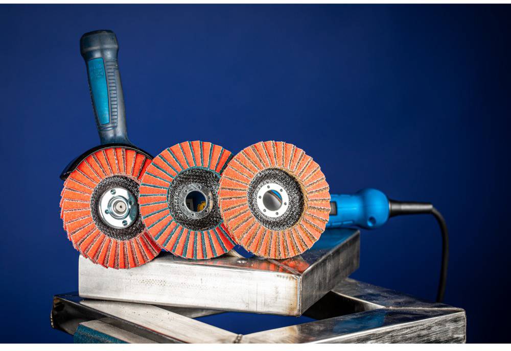 Drei rot-schwarze Schleifscheiben auf einem Metallblock vor blauem Hintergrund. Eine Schleifscheibe hat einen blauen Griff.