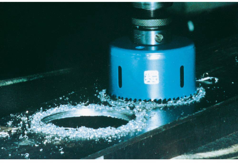 Sägeblatt schneidet ein rundes Loch in eine Metallplatte, umgeben von metallischen Spänen.