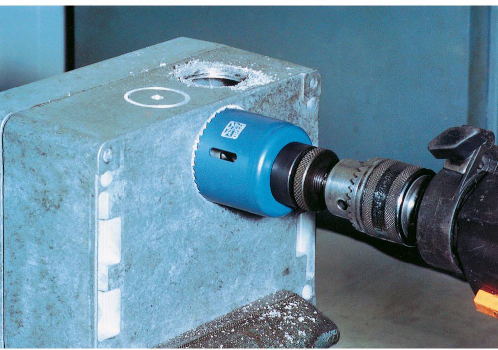 Eine blaue Lochsäge schneidet ein rundes Loch in ein graues Metallgehäuse. Eine schwarze Bohrmaschine ist an der Säge befestigt.