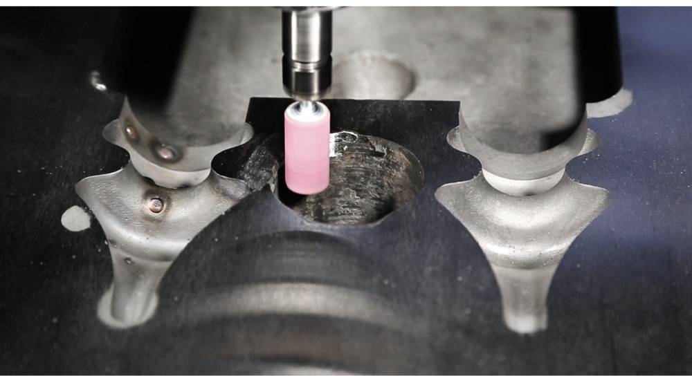 Nahaufnahme einer Fräsmaschine, die präzise Metall bearbeitet. Der Fräskopf ist rosa und arbeitet an einem dunklen Metallstück.