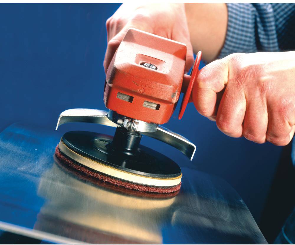 Eine Person schleift eine Metalloberfläche mit einer elektrischen Poliermaschine. Die Maschine hat einen roten Griff.