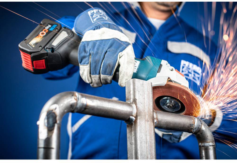 Person in blauer Arbeitskleidung schleift Metallrohr mit Winkelschleifer, Funken sprühen.