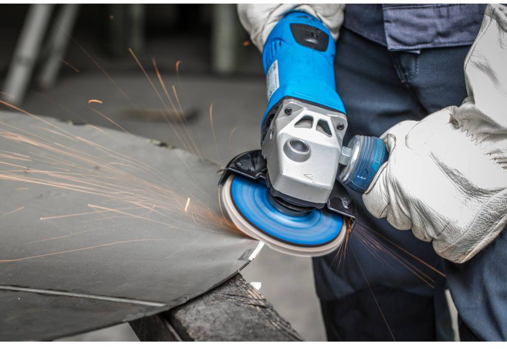 Arbeiter mit blauen Handschuhen schleift Metall mit einer blauen Winkelschleifmaschine, Funken fliegen.