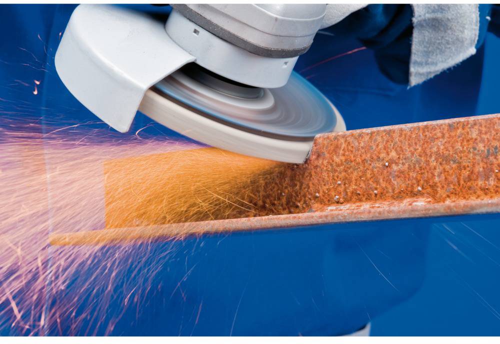 Eine Schleifmaschine bearbeitet ein rostiges Metallstück, dabei fliegen Funken. Die Hauptaktion ist das Schleifen von Metall.
