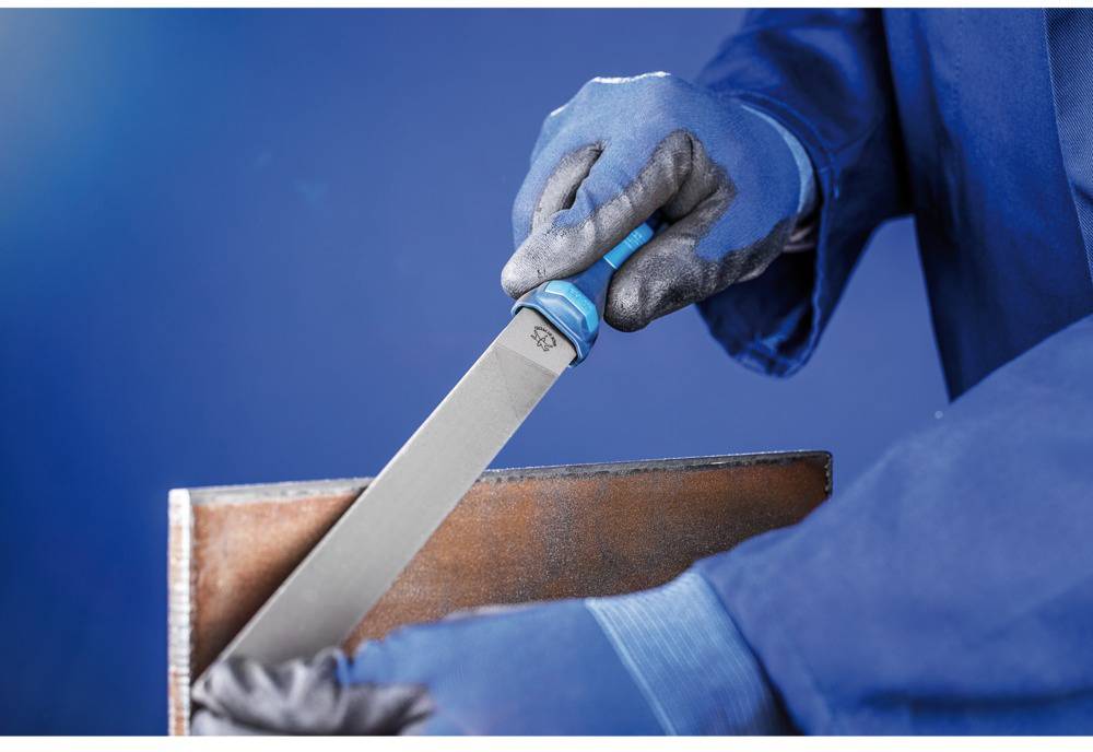 Eine Person in blauer Schutzkleidung feilt eine Metallkante mit einer Feile. Hände sind mit blauen Handschuhen geschützt.