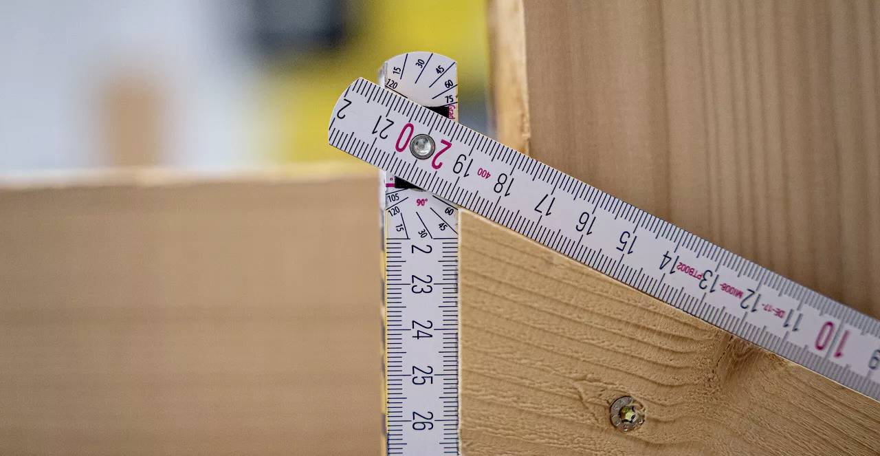 Ein Maßband zeigt 27 cm bei einem Holzstück in einem 90-Grad-Winkel. Es dient zur Vermessung und Konstruktion.