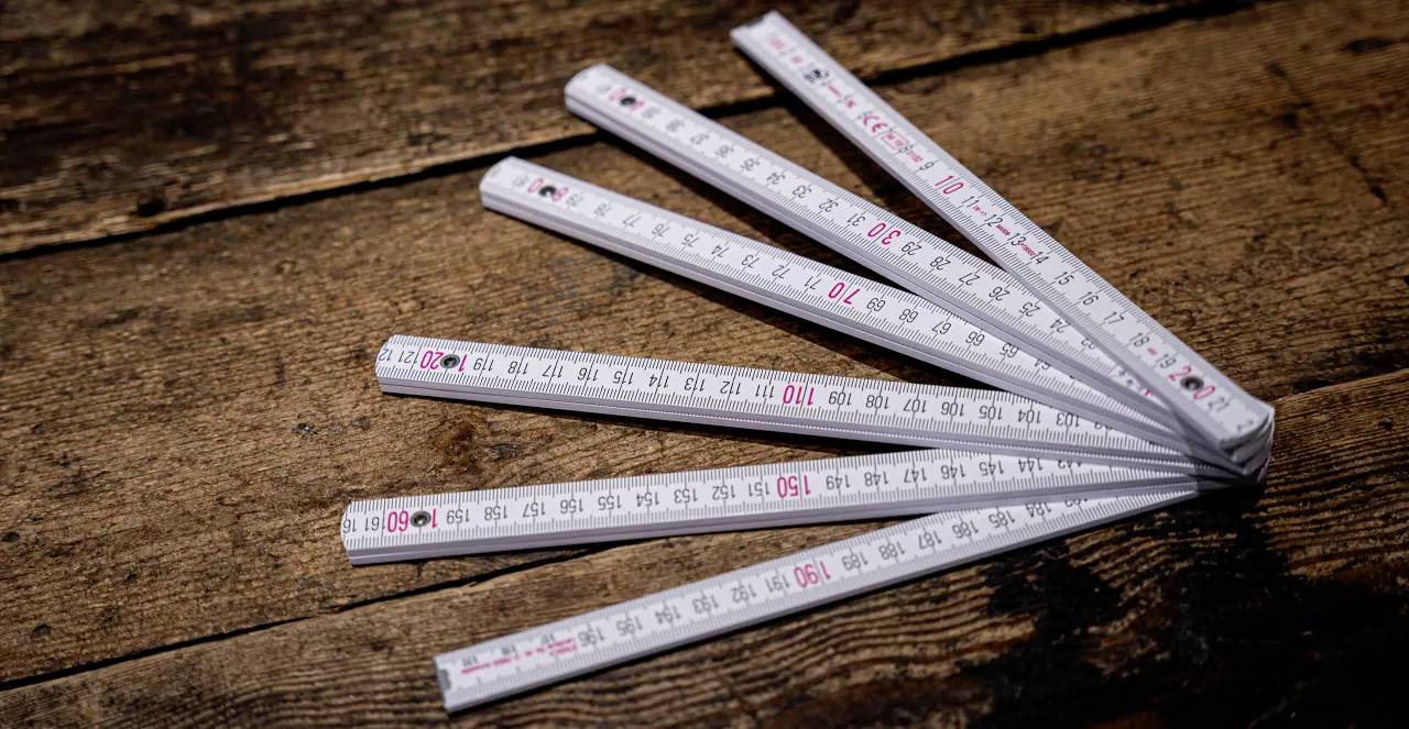 Ein auf einem Holztisch liegender ausgebreiteter weißer Gliedermaßstab mit roten und schwarzen Markierungen.