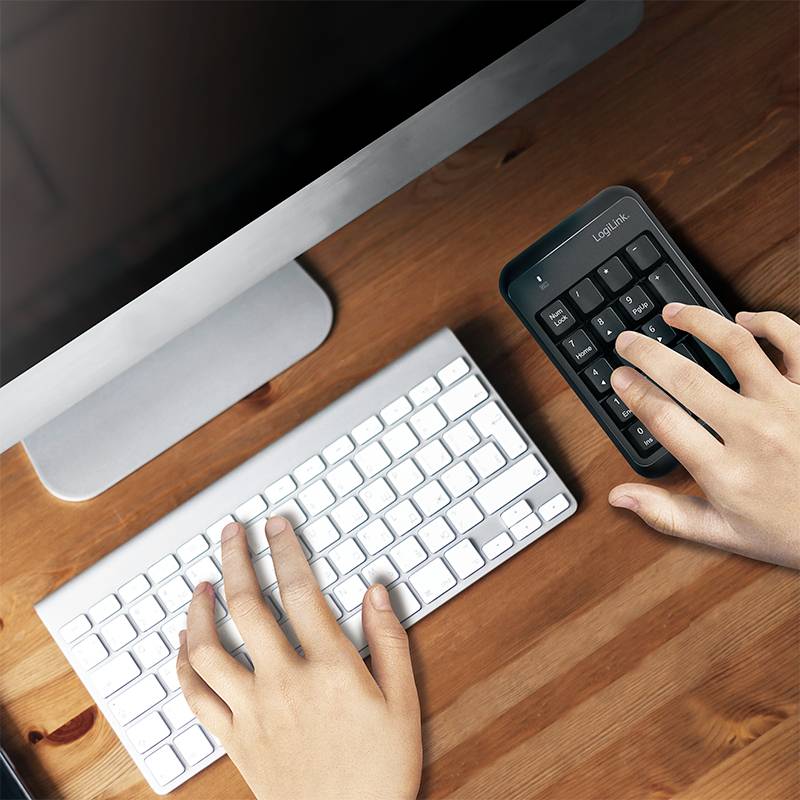 Eine Person tippt auf einem separaten Nummernblock neben einer Computertastatur. Der Monitor ist im Hintergrund sichtbar.