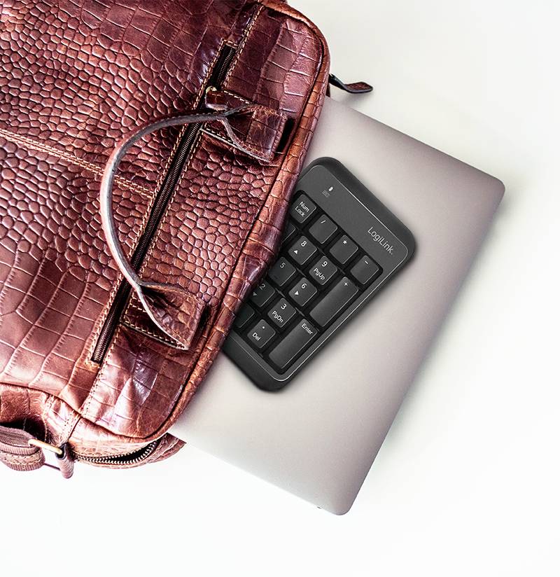 Eine braune Ledertasche liegt auf einem geschlossenen Laptop. Ein Nummernblock mit der Aufschrift 'LogiLink' liegt teilweise auf dem Laptop.