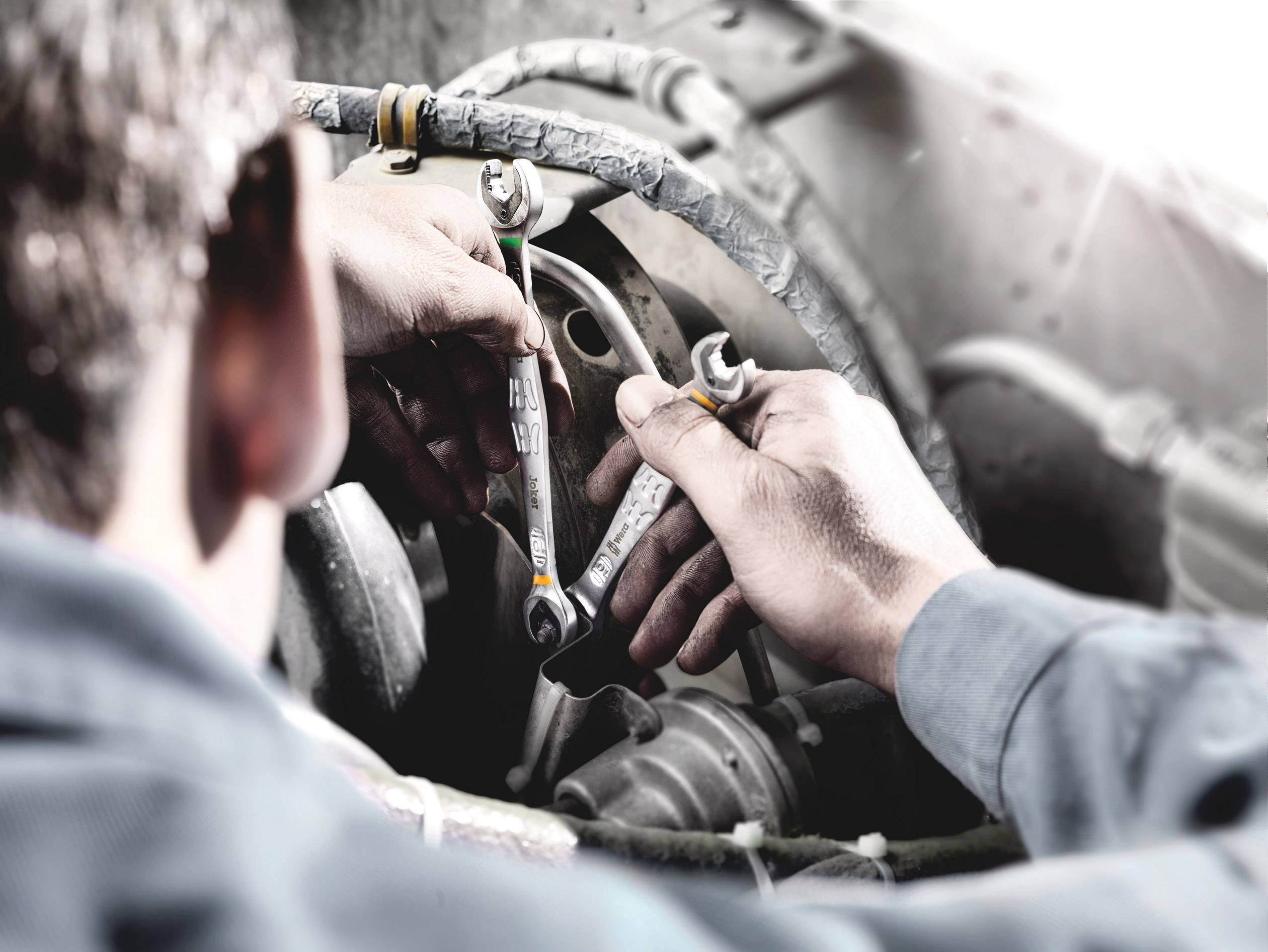 Ein Mechaniker repariert einen Motor, indem er zwei Schraubenschlüssel verwendet. Hände konzentrieren sich auf präzise Arbeit im Motorraum.