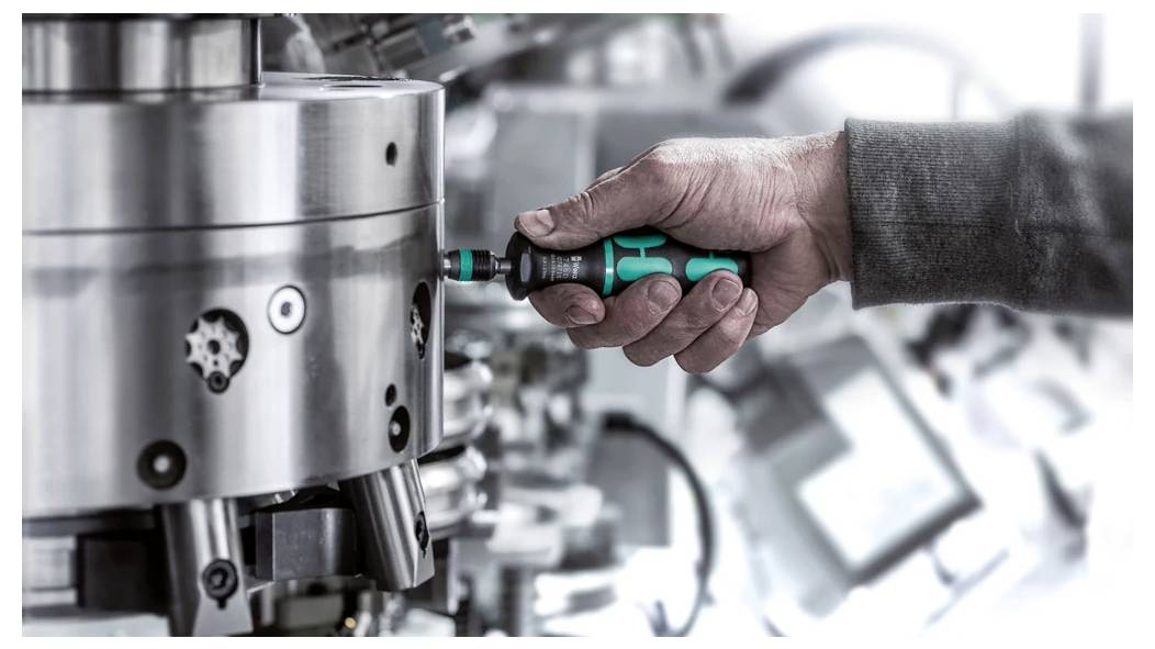 Nahaufnahme einer Person, die einen Schraubendreher verwendet, um eine Metallmaschinenkomponente in einer Industriewerkstatt anzupassen.