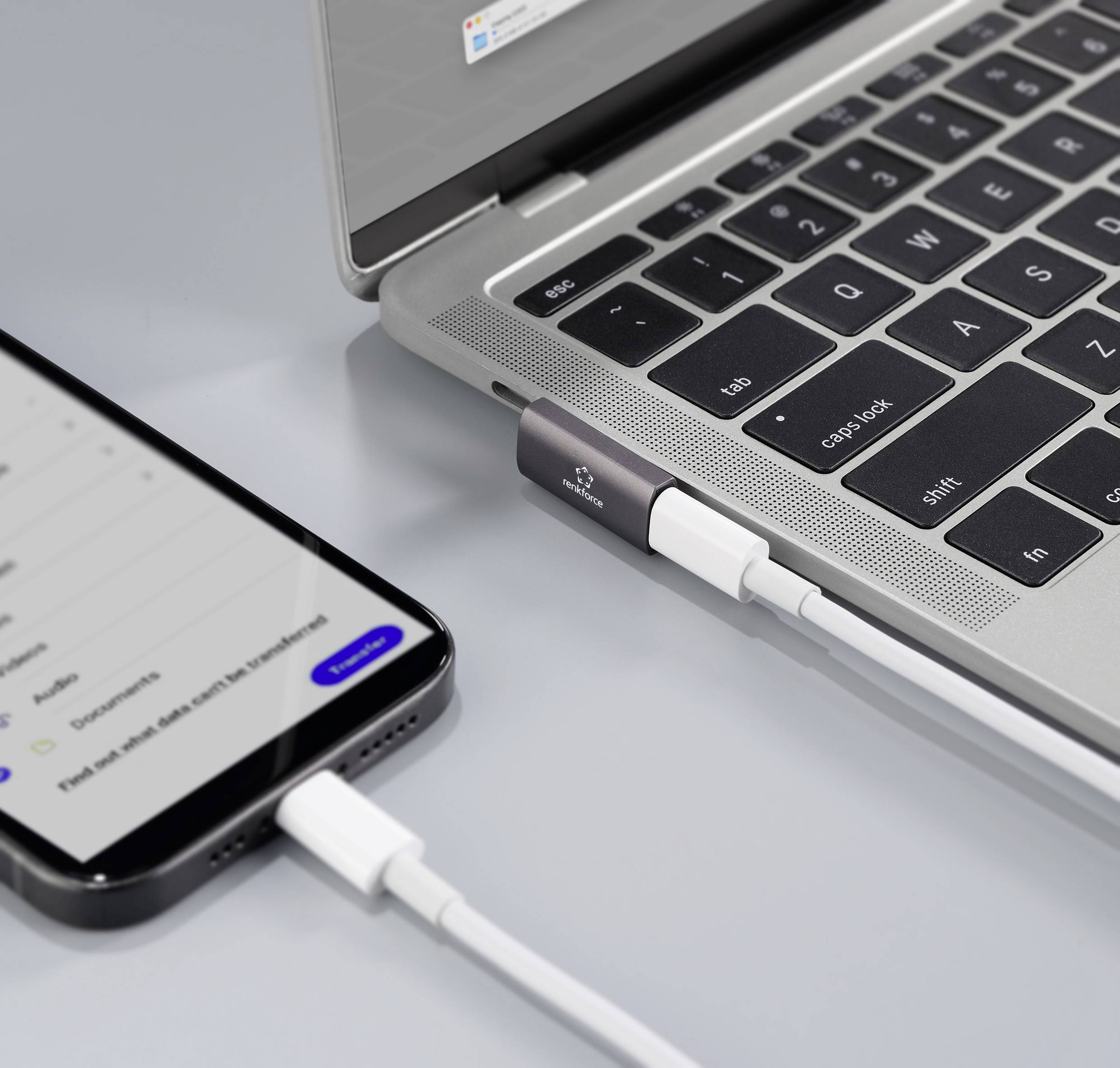 Ein Smartphone ist mit einem Kabel an einen Laptop angeschlossen, der auf einem Tisch liegt. Der Laptop-Bildschirm zeigt einen Ladebildschirm.