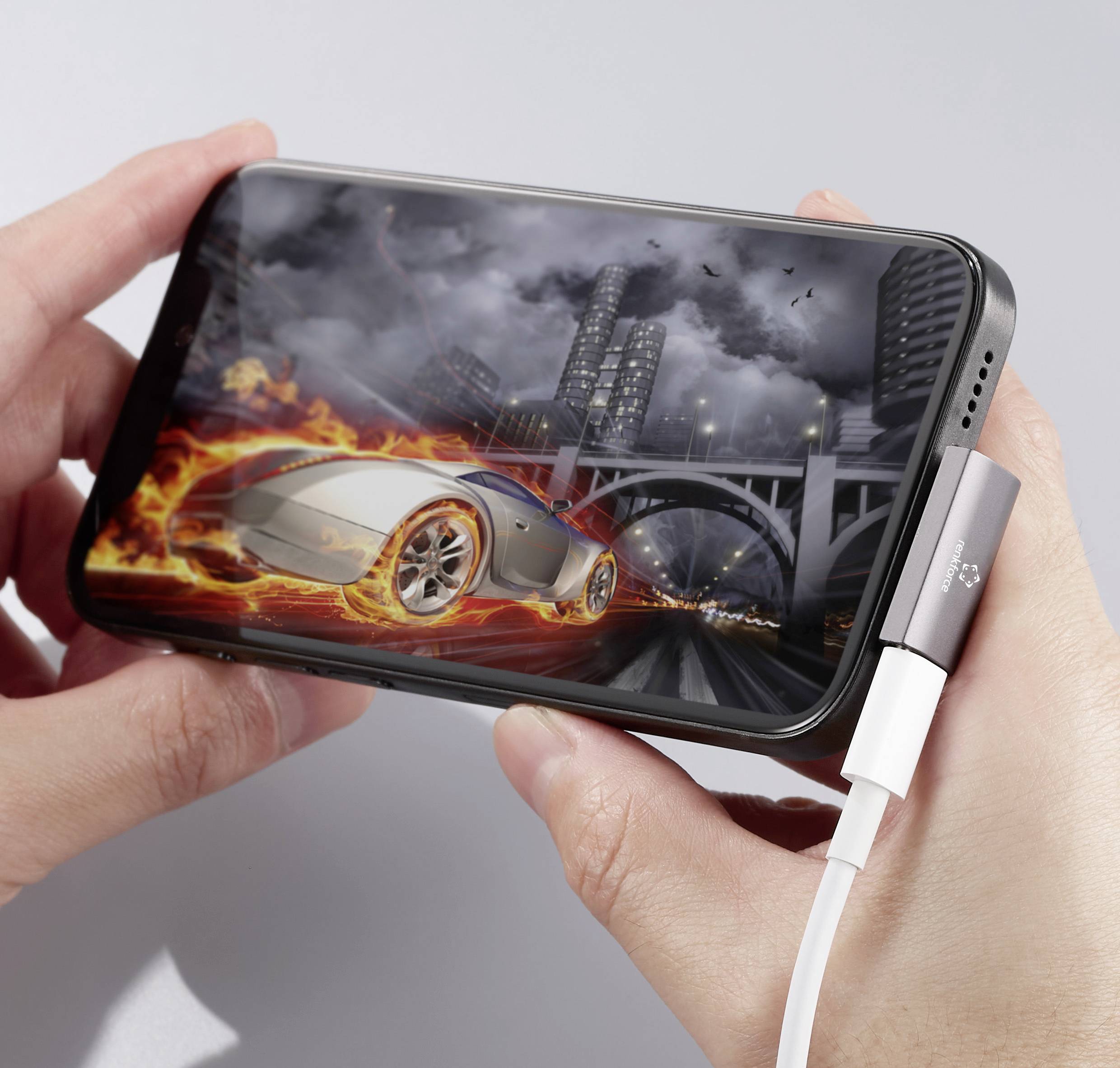 Mensch hält Smartphone mit Rennspiel, zeigt flammenbedecktes Auto auf Stadtstraße, während es Aufladegerät angeschlossen ist.