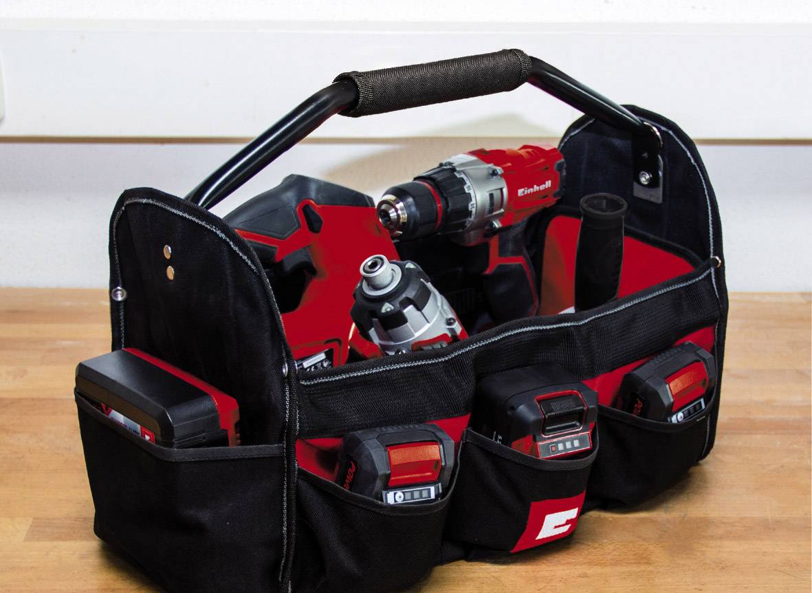 Eine schwarze Werkzeugtasche mit verschiedenen roten Elektrowerkzeugen und Batterien auf einem Holztisch.