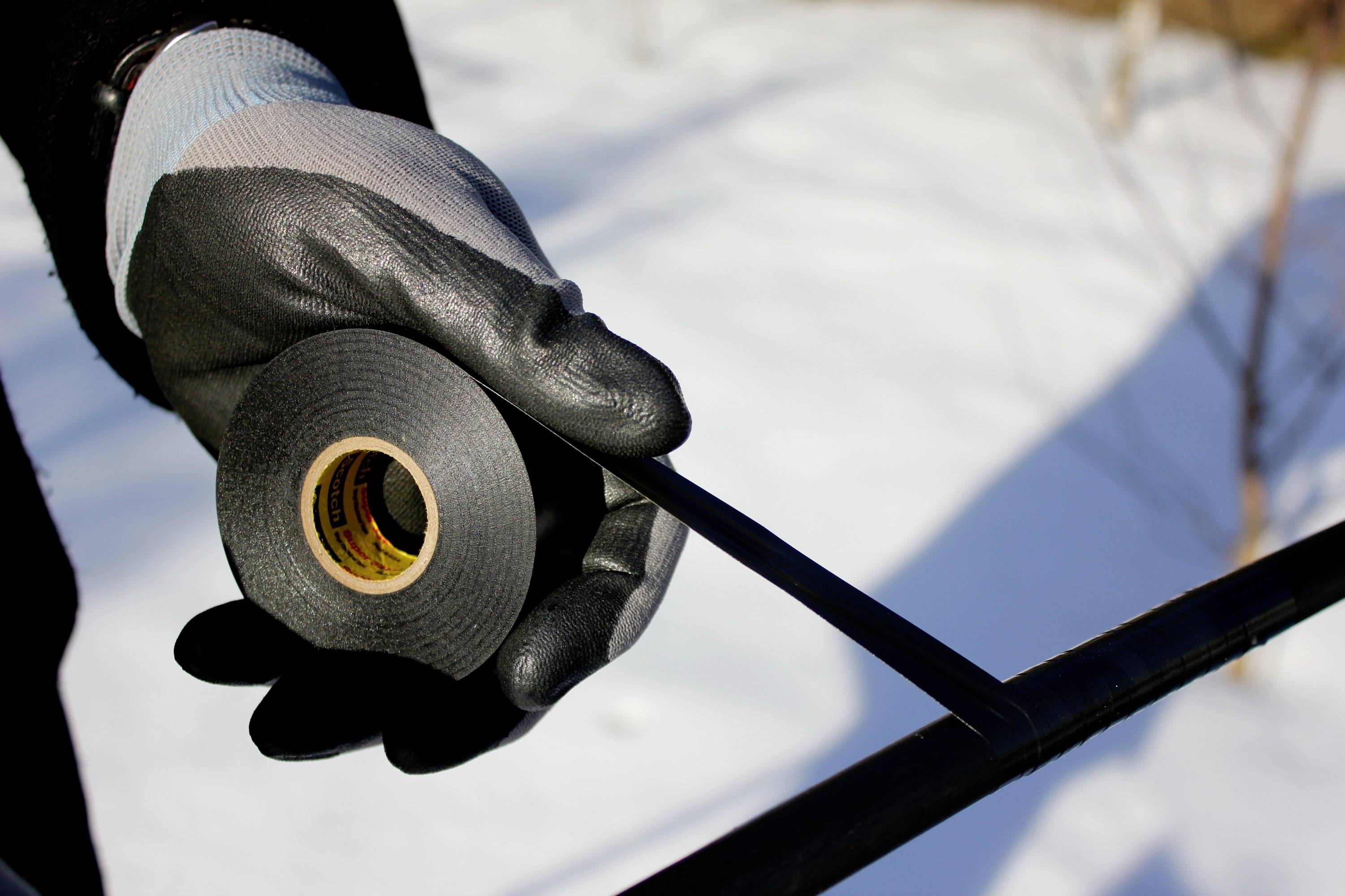 Eine behandschuhte Hand hält Isolierband und umwickelt ein Kabel im Freien. Hintergrund zeigt Schnee.