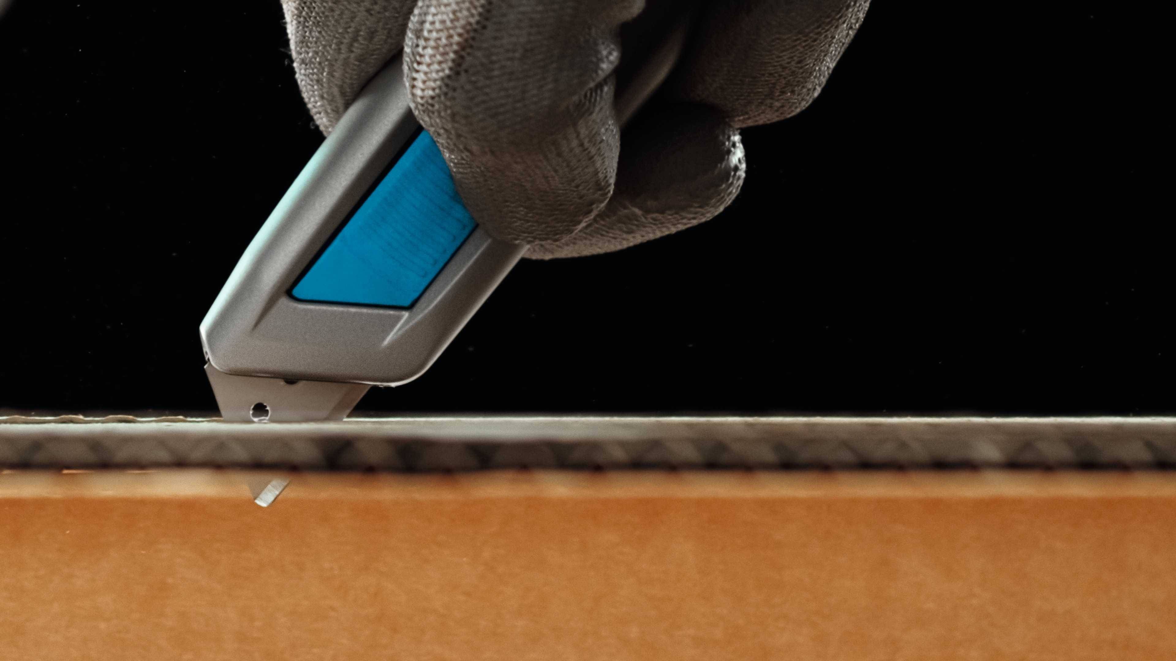 Eine Hand mit Handschuh schneidet mit einem Cuttermesser Karton.