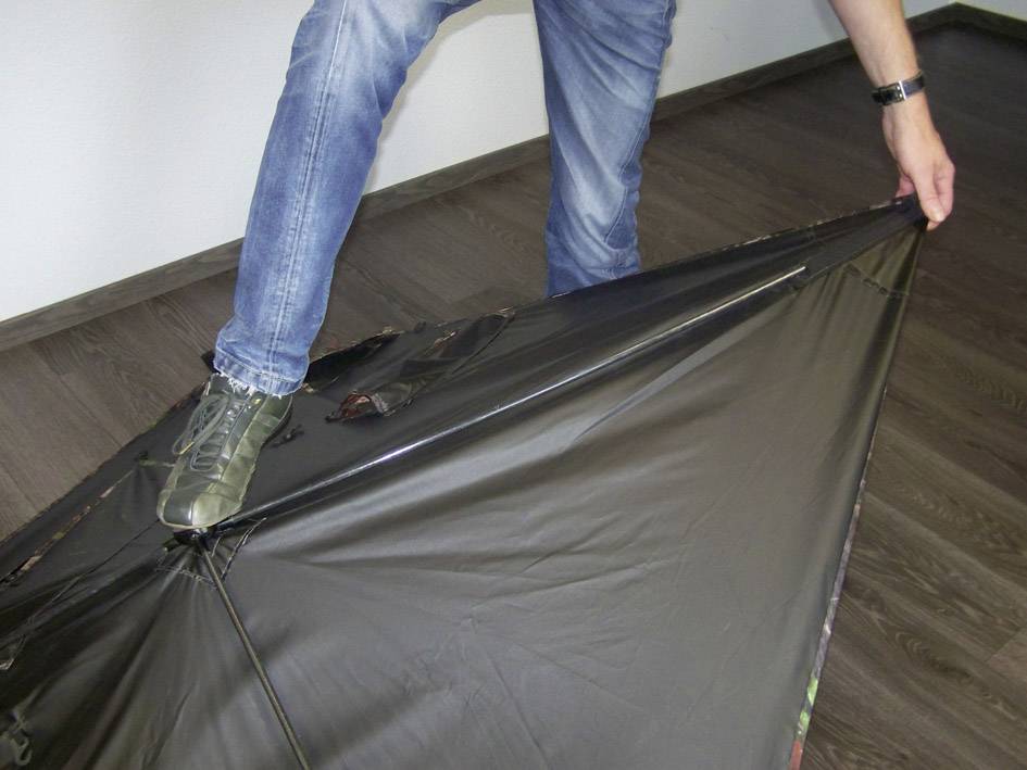 Eine Person drückt mit einem Schuh auf einen großen, schwarzen Regenschirm, der sich auf dem Boden befindet.