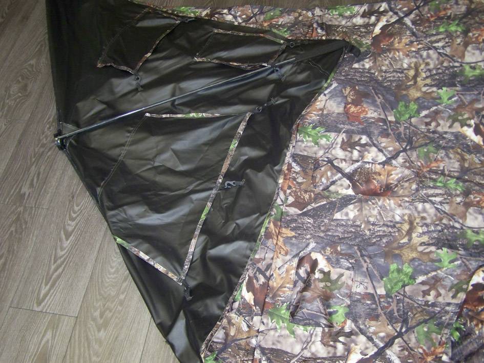 Ein Zelt mit Tarnmuster liegt auf einem Holzboden. Ein schwarz glänzendes Stoffelement zeigt eine geschlossene Reißverschlussöffnung.