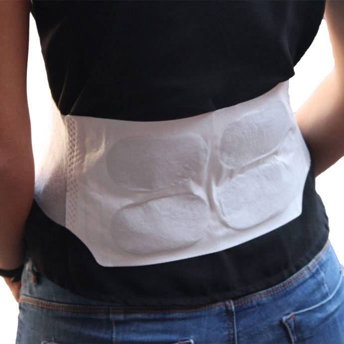 Eine Person trägt einen weißen Rückenwärmer oder Heizkissen unter einem schwarzen T-Shirt, das um die Taille geschnallt ist.