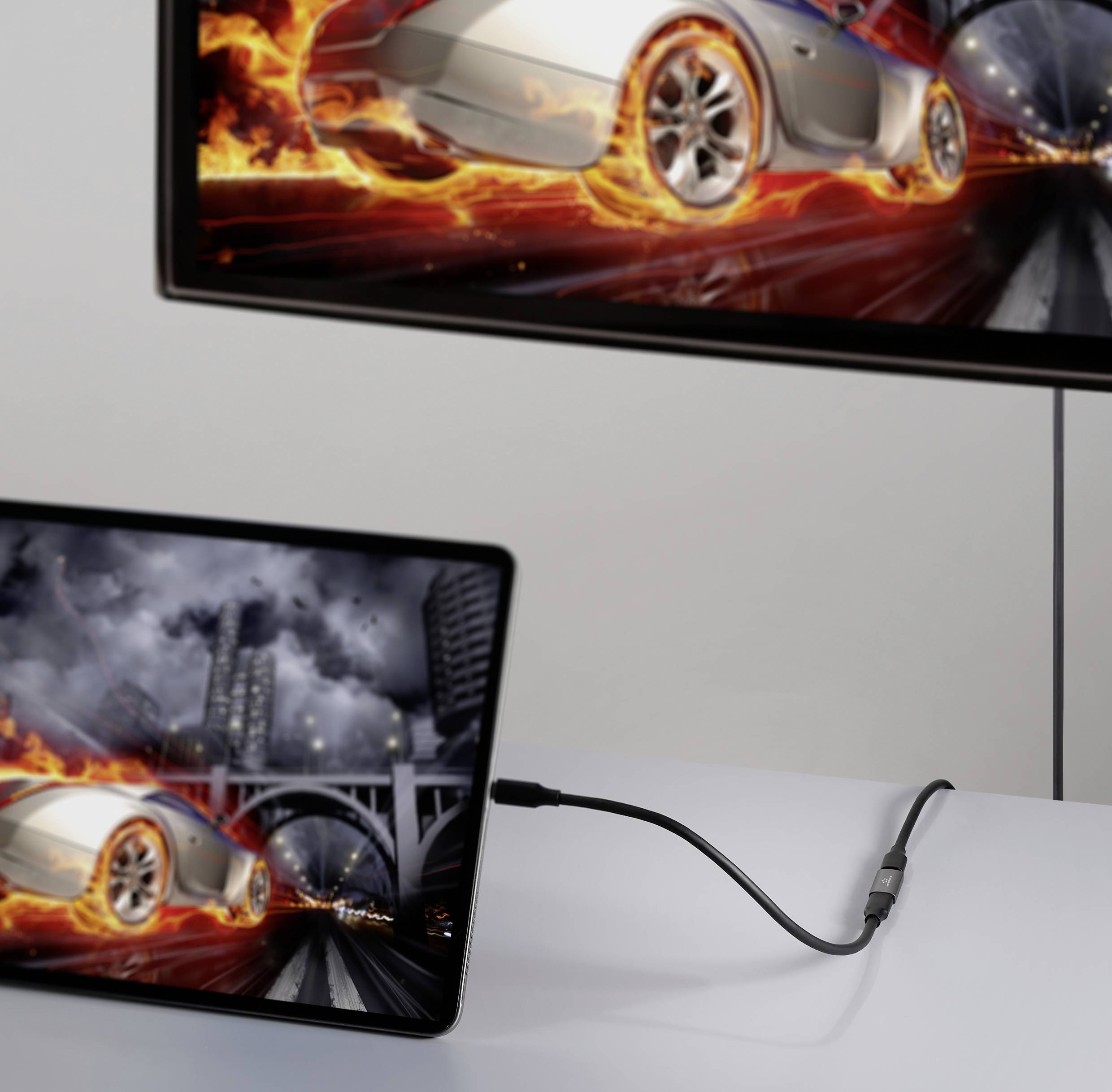 Ein Tablet zeigt ein Bild eines Autos mit Flammeneffekten. Es ist mit einem Kabel an einen größeren Bildschirm angeschlossen, der dasselbe Bild zeigt.