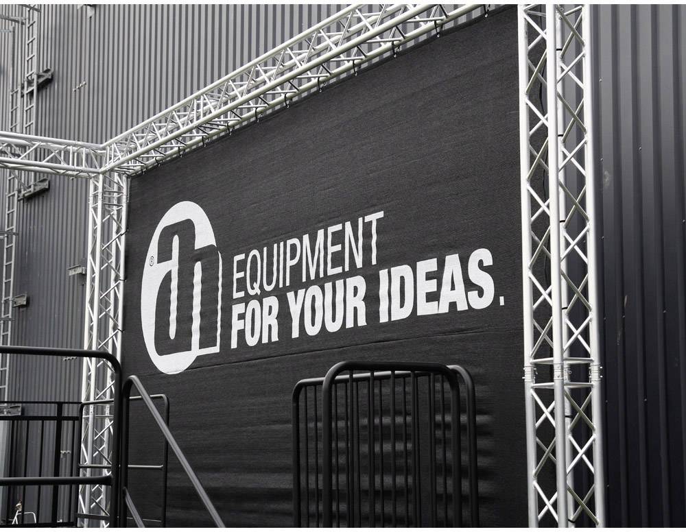 Schwarze Wand mit großem Text 'EQUIPMENT FOR YOUR IDEAS' in weiß. Umgeben von einem silbernen Gerüst.