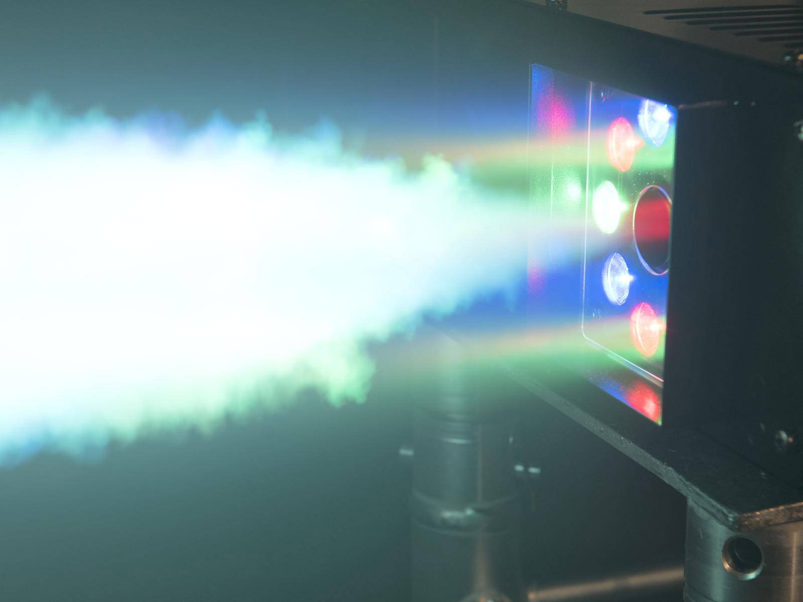 Laserprojektor mit bunten Lichtstrahlen in einem dunklen Raum. Es wird grünes, blaues und rotes Licht deutlich sichtbar emittiert.