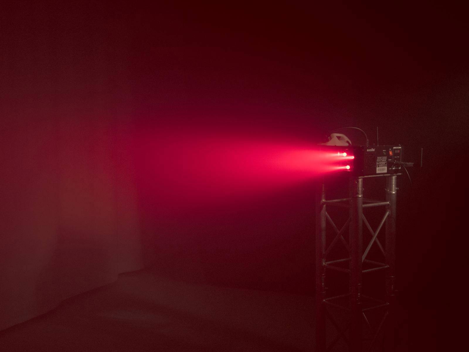 Ein roter Laserstrahl wird von einem Projektor in einem dunklen Raum ausgestrahlt, der auf einem Metallgestell montiert ist.