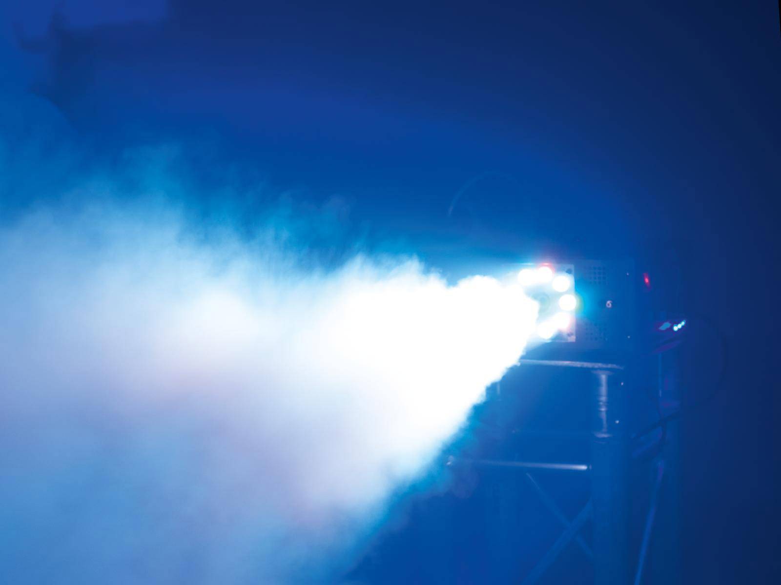 Ein starker blauer Lichtstrahl von einem Scheinwerfer beleuchtet die Szene, umgeben von Nebel und Dunkelheit.