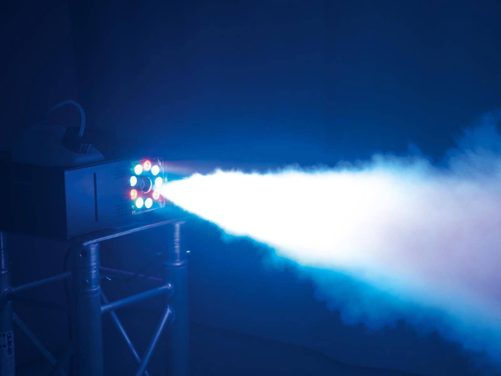 Nebelmaschine produziert hellen Lichtstrahl in dunkler Umgebung, montiert auf Metallstativ. Lichtkegel und Nebel sind sichtbar.