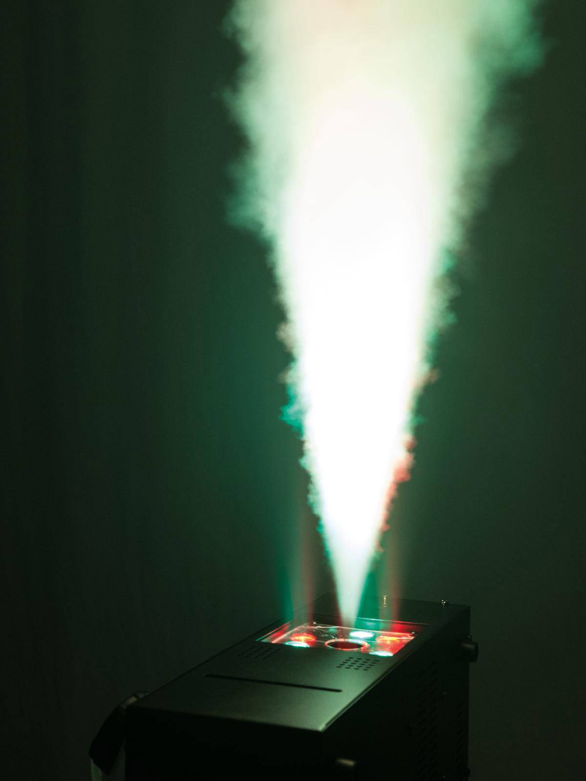 Eine Nebelmaschine stößt einen weißen Lichtstrahl mit roten und grünen Akzenten in die Luft, vor dunklem Hintergrund.