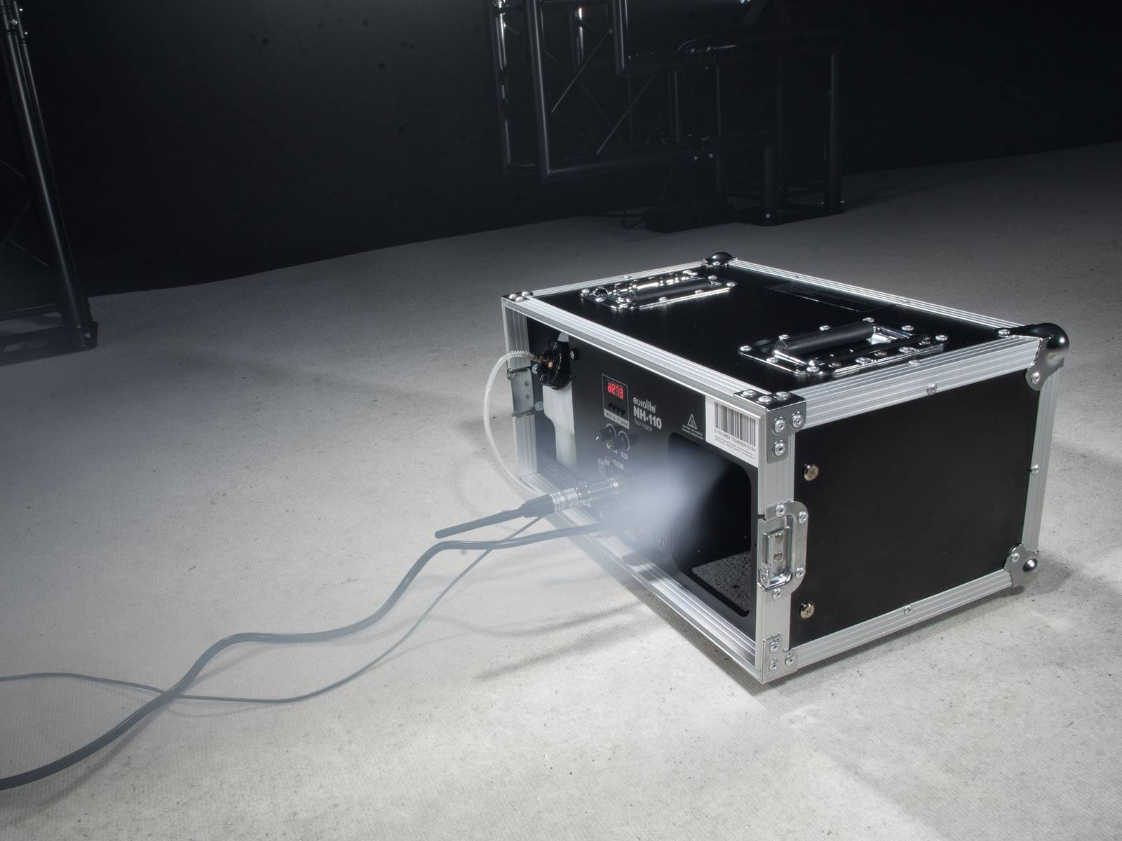 Ein Nebelgerät auf einem Boden setzt Dunst frei, Kabel führen zum Gerät. Es wird oft in Bühnenproduktionen verwendet, um Effekte zu erzeugen.