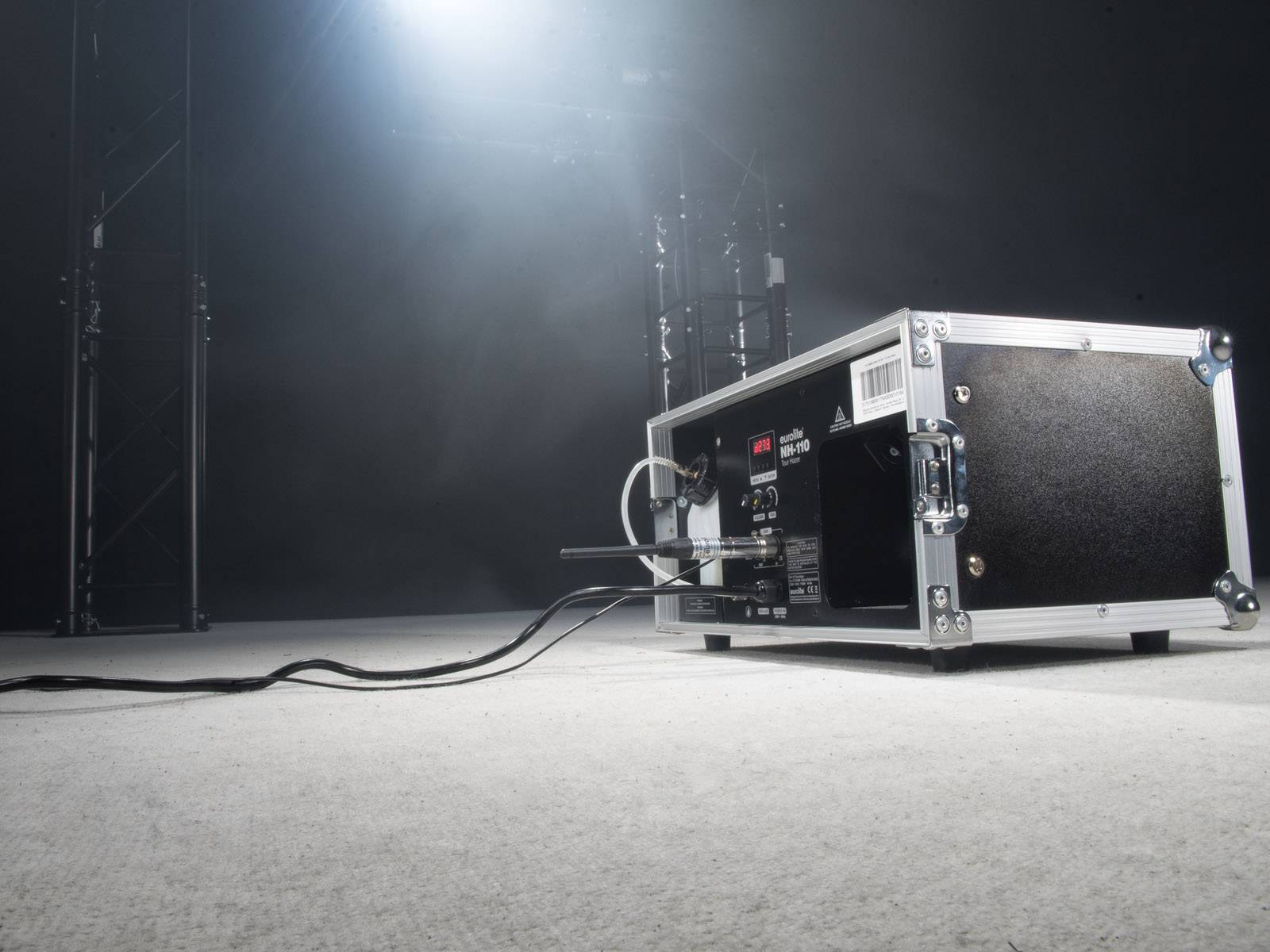 Ein schwarzer Elektrokasten mit Kabeln auf einem grauen Boden in einem dunklen Raum. Diffuses Licht leuchtet von oben.