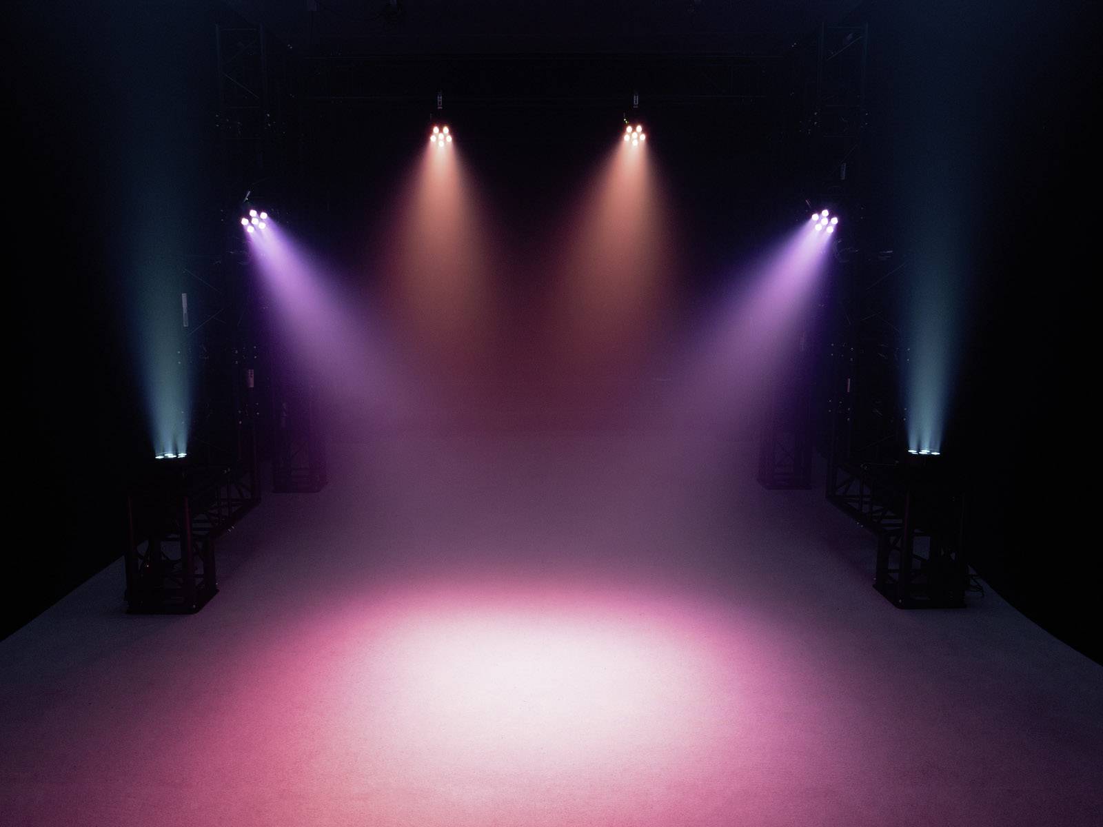 Bühne mit bunten Scheinwerfern, die von oben herab leuchten und einen leeren Raum in rötlichem und violettem Licht bestrahlen.