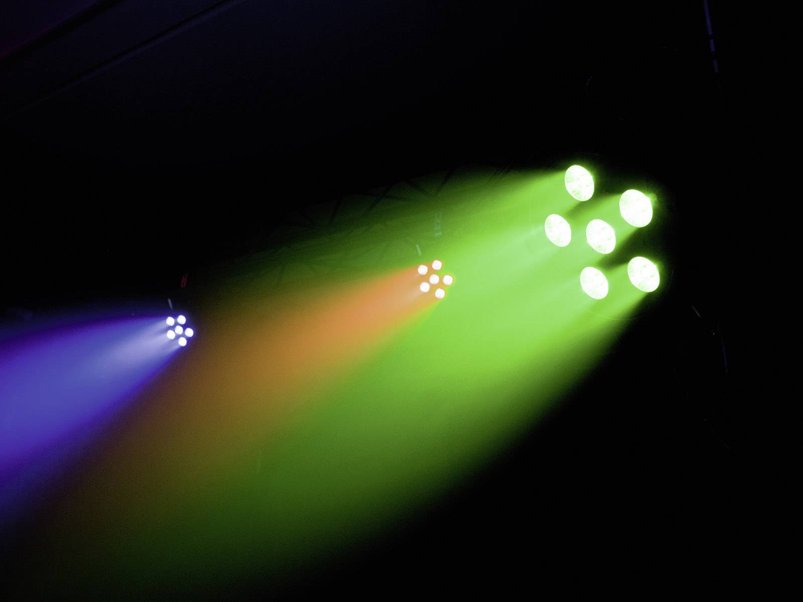 Farbenfrohe Scheinwerfer strahlen in Blau, Orange und Grün von rechts nach links in einem dunklen Raum, schaffen lebendige Lichteffekte.