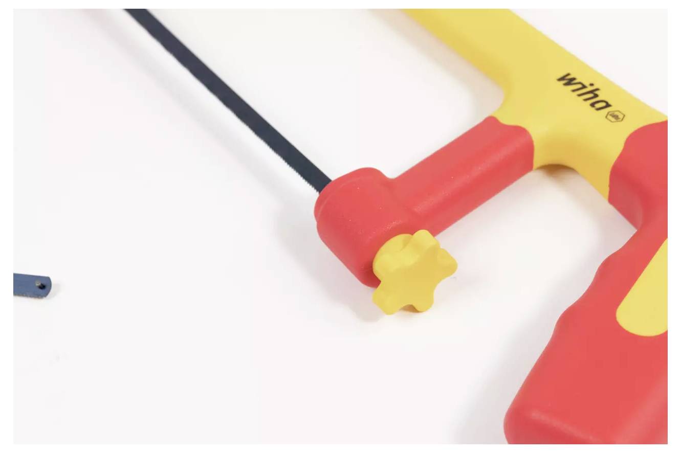 Eine rot-gelbe Handsäge mit schwarzem Blatt, teilweise sichtbar auf einer weißen Oberfläche, mit Fokus auf ihren Griff und die Spannknopf.