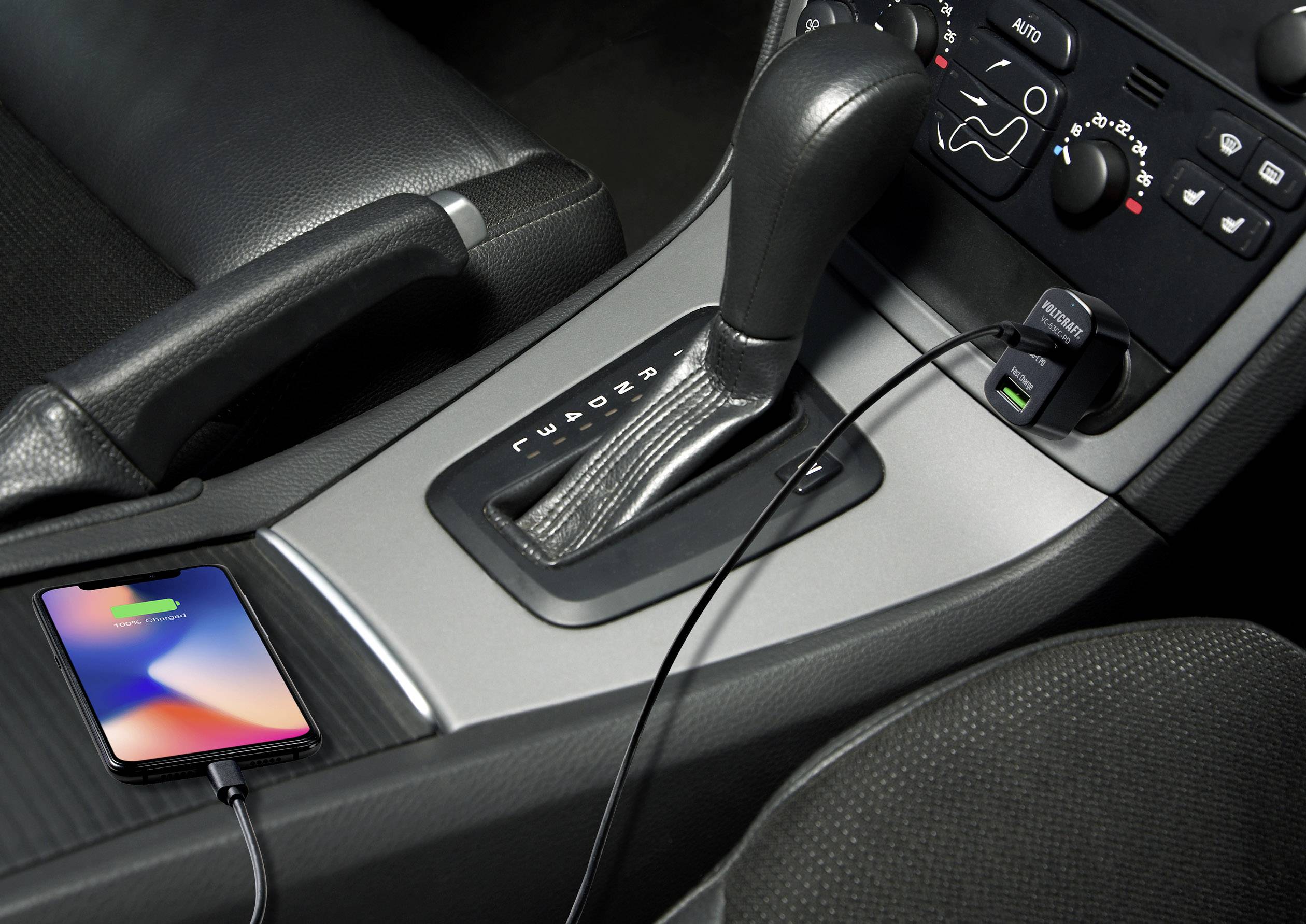Ein Smartphone wird im Auto aufgeladen. Es ist mit einem Kabel an die USB-Buchse neben dem Schalthebel angeschlossen.