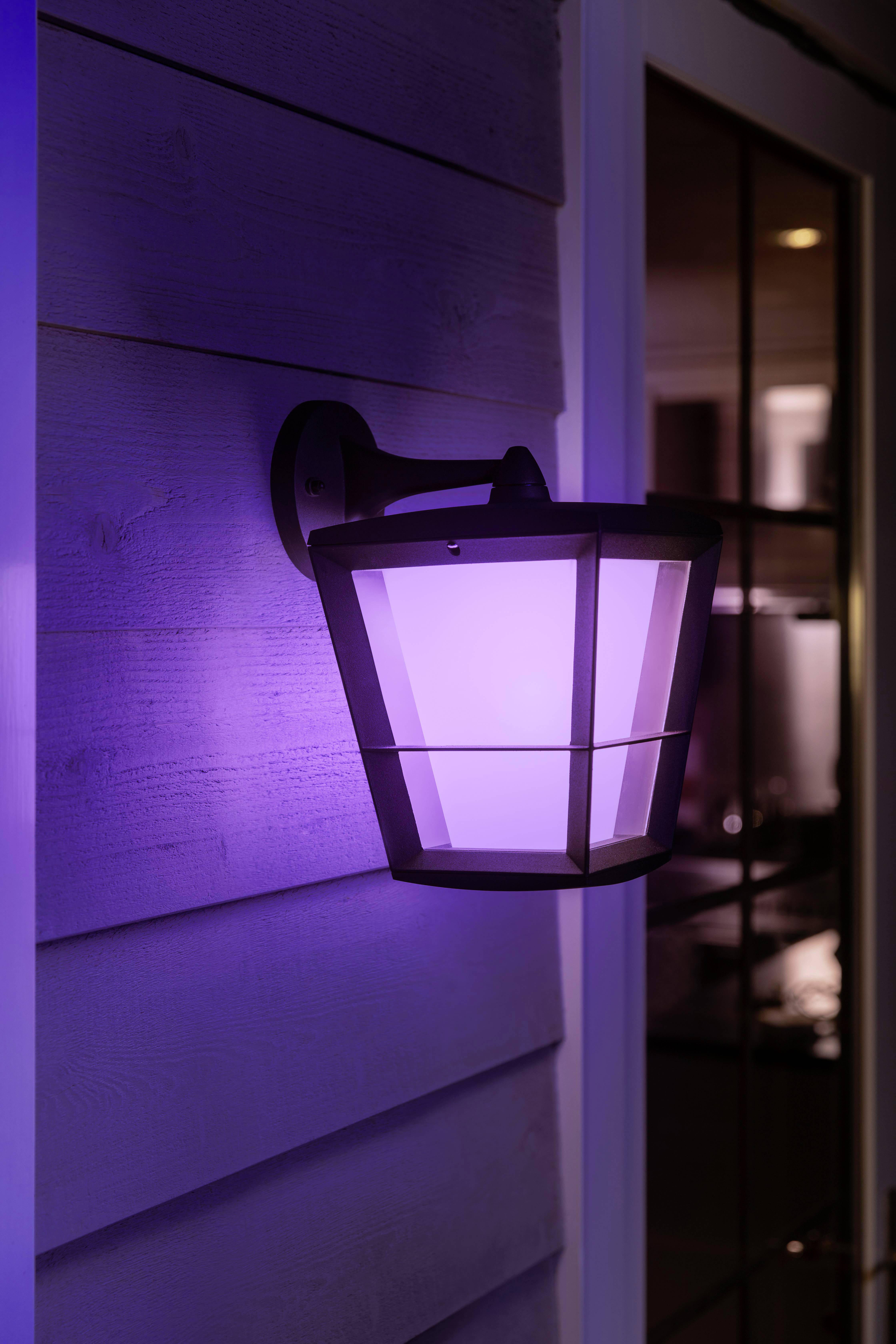Außenwandleuchte an einer Hauswand, leuchtet in violettem Licht.