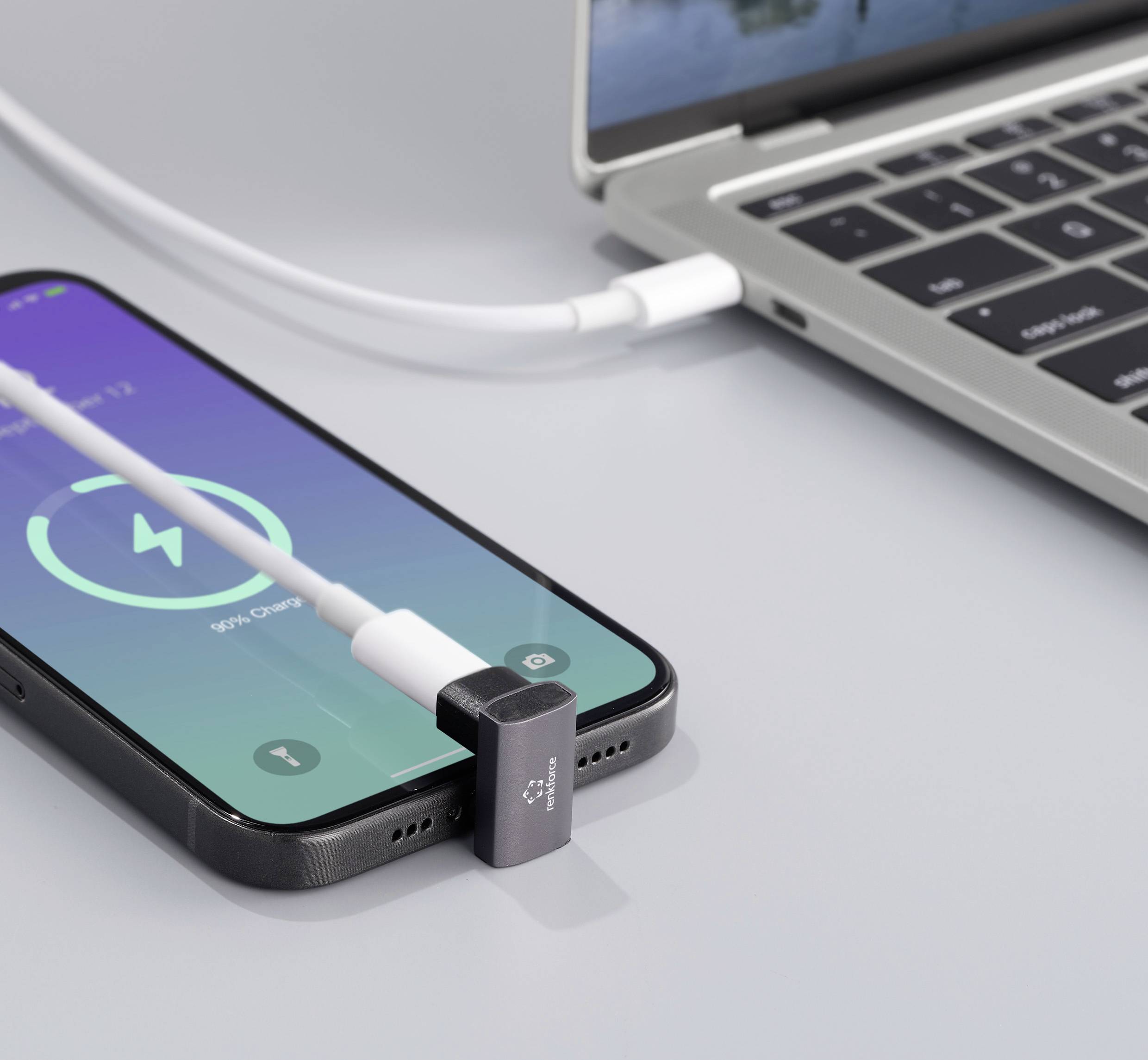 Smartphone lädt neben einem Laptop. Ladekabel ist angeschlossen, und der Bildschirm zeigt 54 % Akkuladung an.