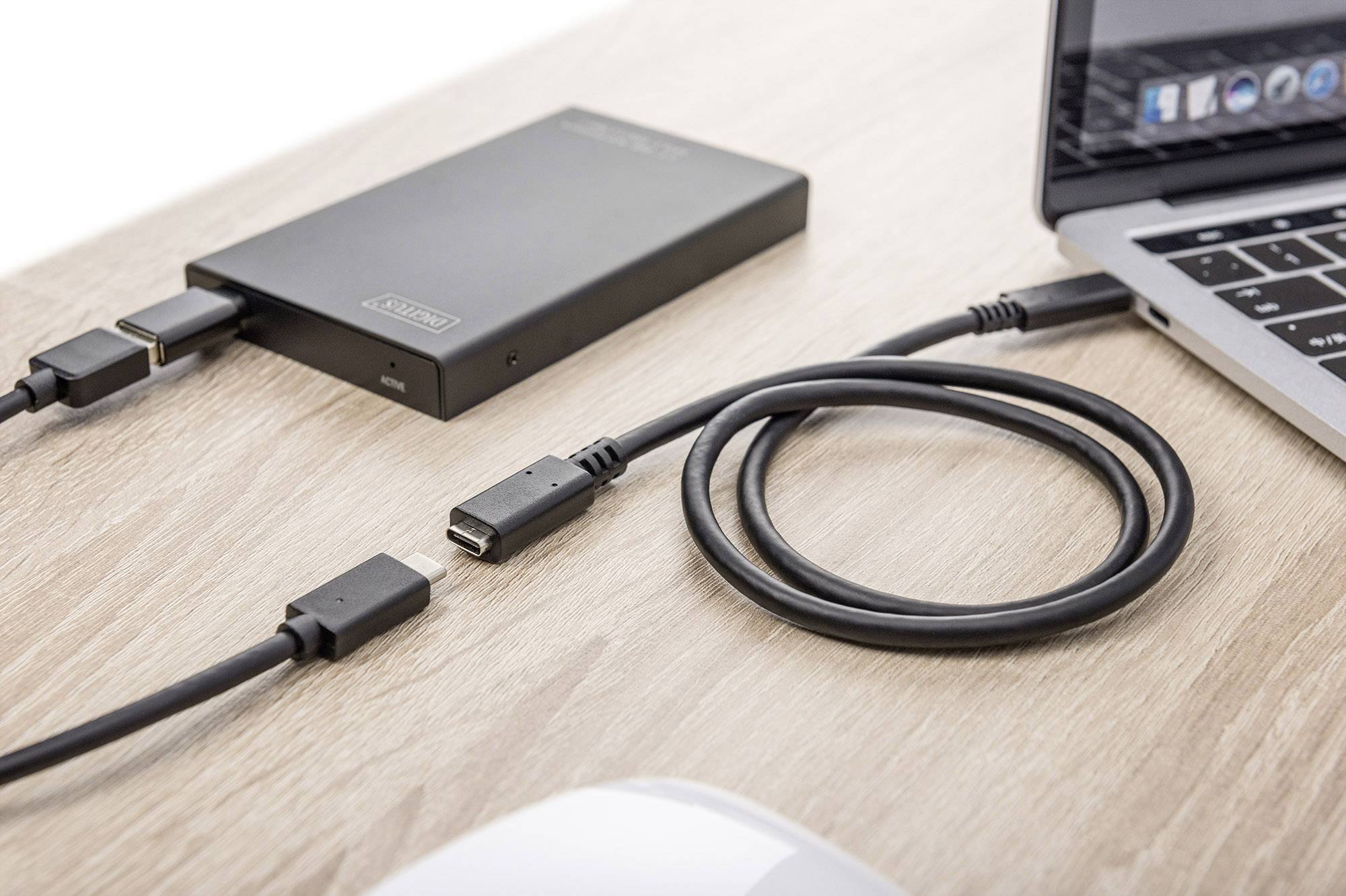 Ein Laptop ist über ein USB-Kabel mit einer externen Festplatte verbunden. Beide Geräte befinden sich auf einem Holztisch.