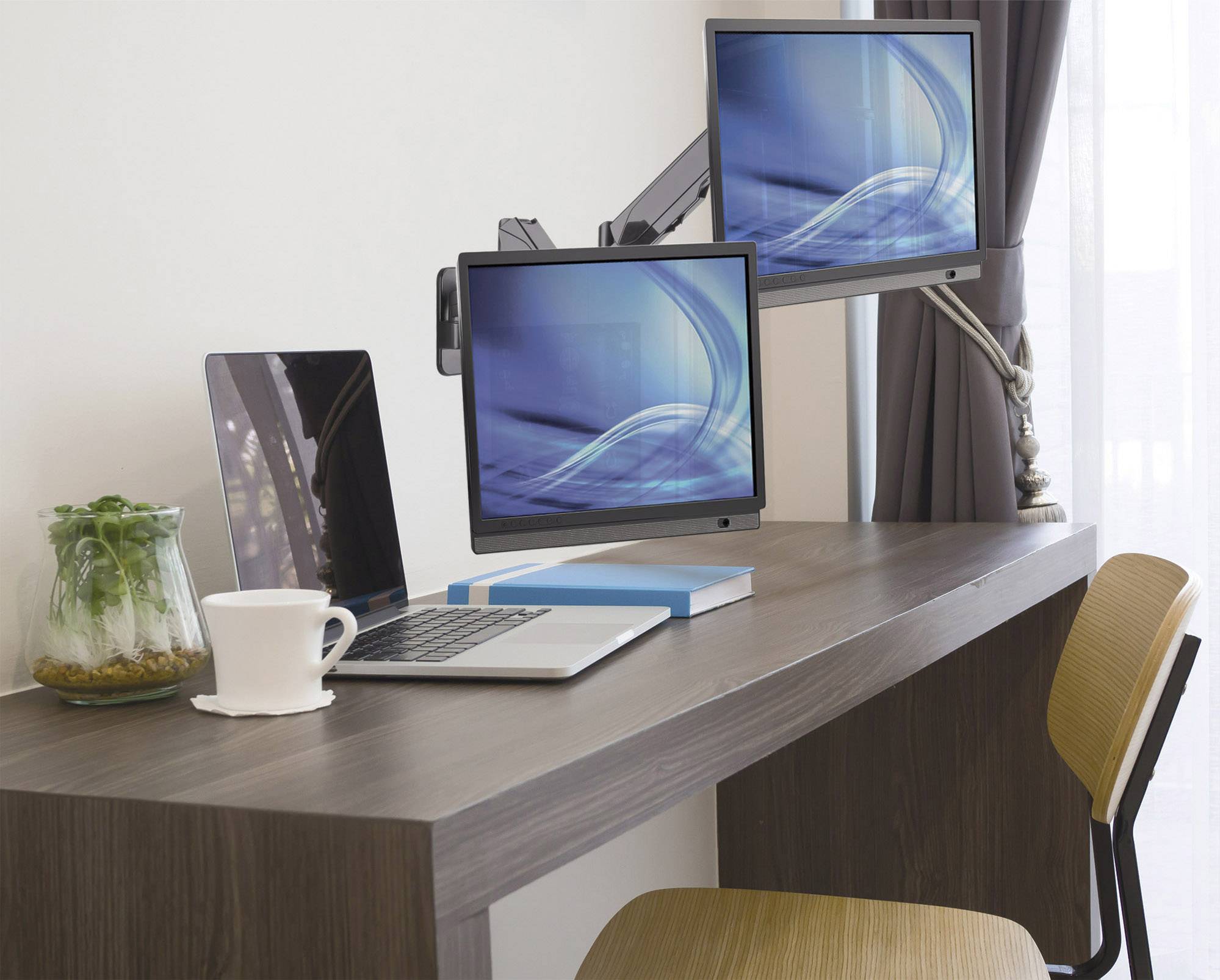 Ein minimalistischer Arbeitsplatz mit einem Laptop, zwei Monitoren, einem Buch, einer Tasse und einer Pflanze auf einem Holztisch.