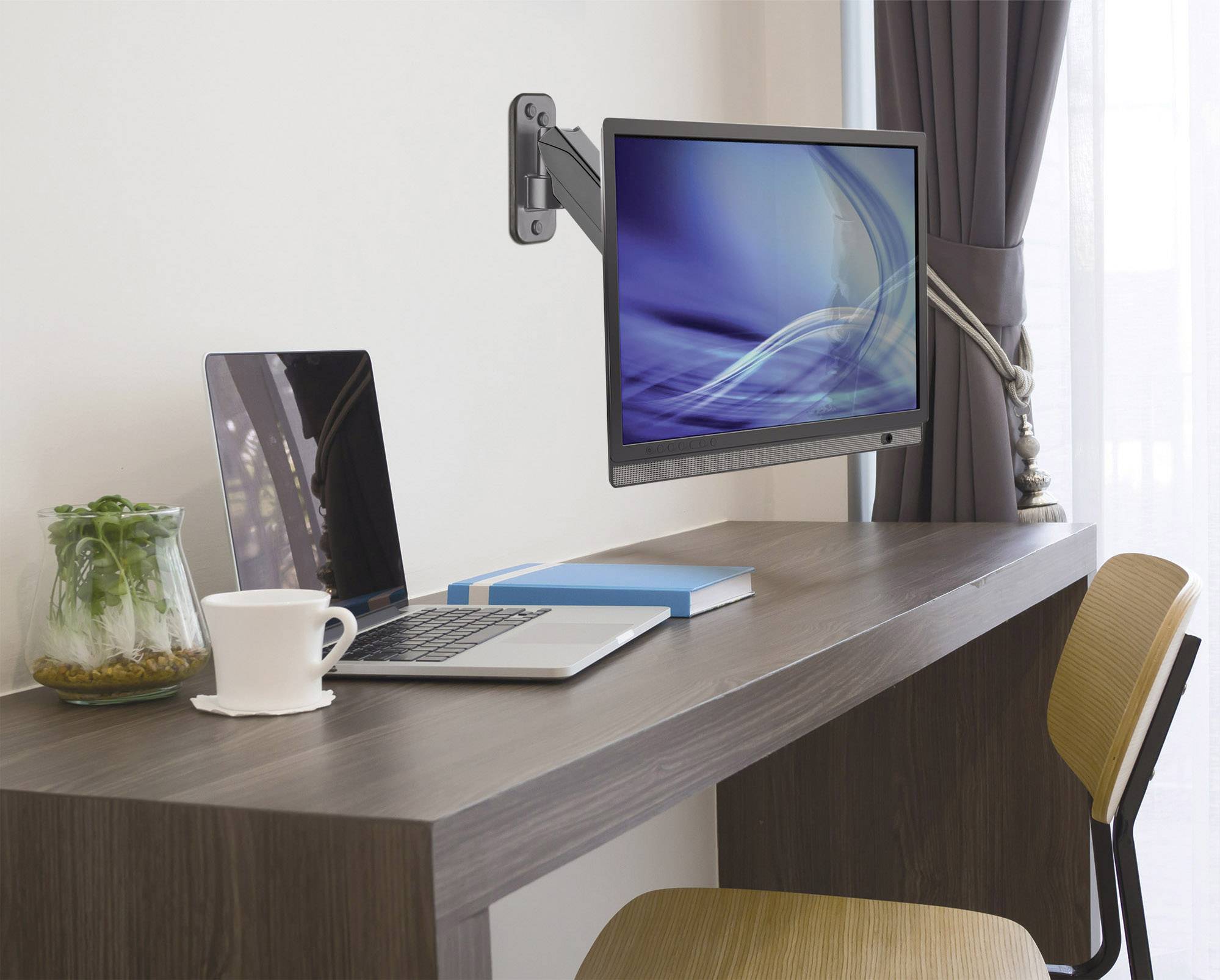 Ein Laptop und ein Monitor an einem Gelenkarm stehen auf einem Schreibtisch. Daneben eine Tasse und ein Glas mit Pflanzen.