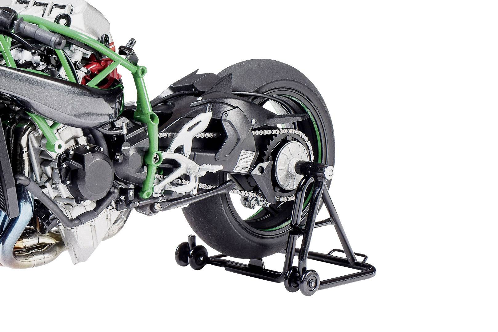 Ein Motorrad mit grünem Rahmen steht auf einem Montageständer, der das Hinterrad stabilisiert. Sichtbar sind Motor- und Kettendetails.