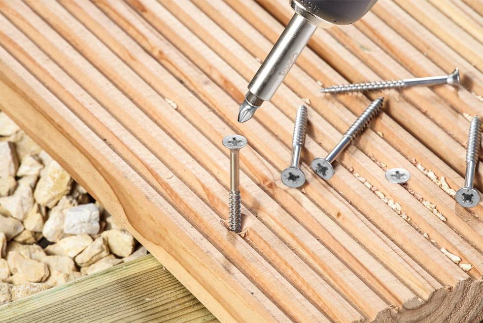 Eine Nahaufnahme einer Holzbearbeitungsszene mit einem Elektroschrauber, der eine Schraube in ein Holzbrett auf Steinen eindreht.