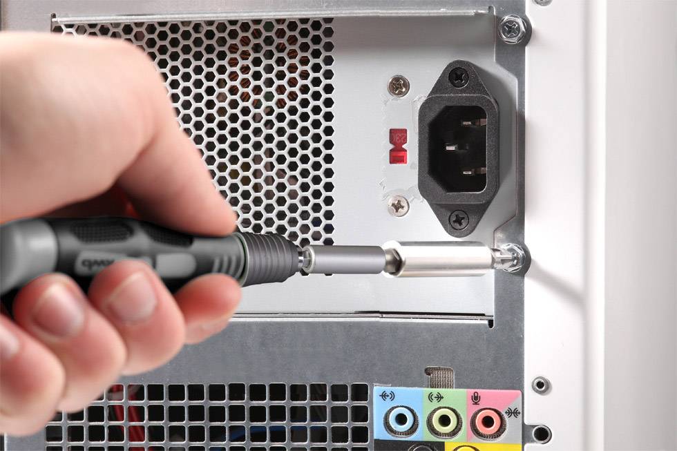 Hand schraubt mit Schraubendreher das Gehäuse eines Computer-Towers auf. Sichtbare Rückseite zeigt Anschlüsse und Stromversorgung.