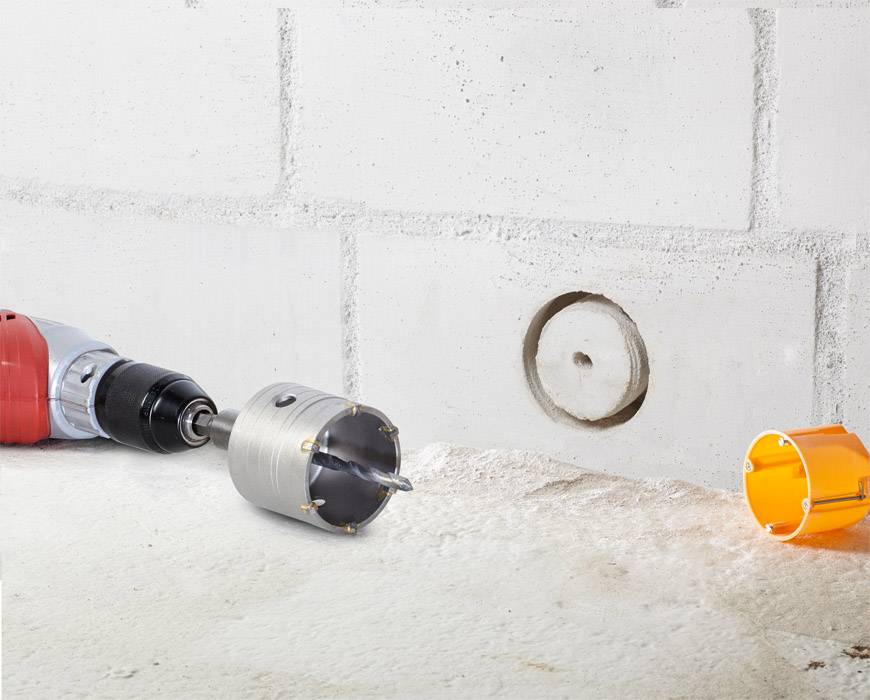Bohrmaschine mit Lochsäge, die ein Loch in eine Betonwand bohrt; Betonstaub und Loch im Vordergrund sichtbar.