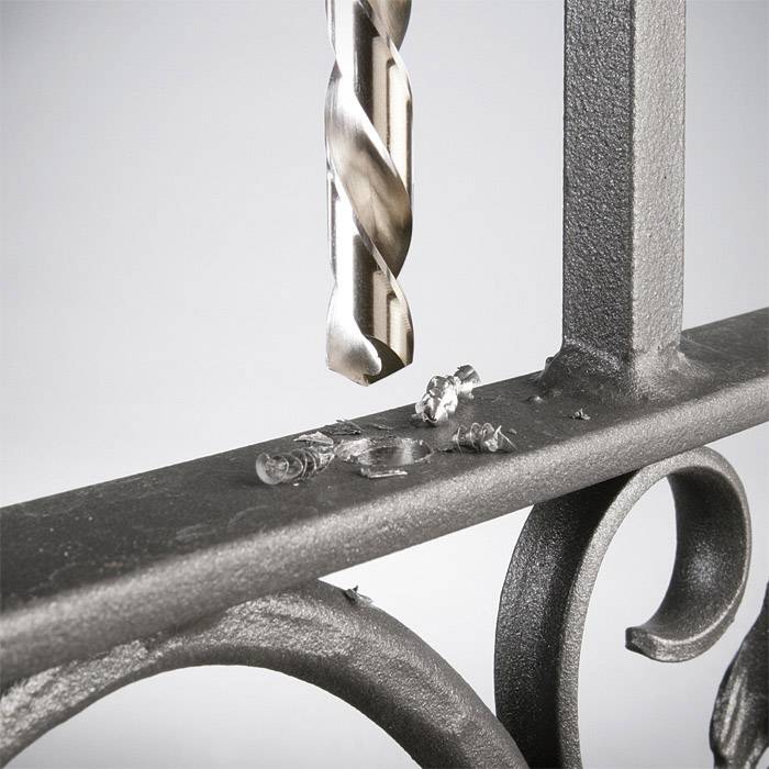 Ein Bohrer bohrt in ein Metallgeländer, Metallspäne verteilen sich um das Bohrloch.