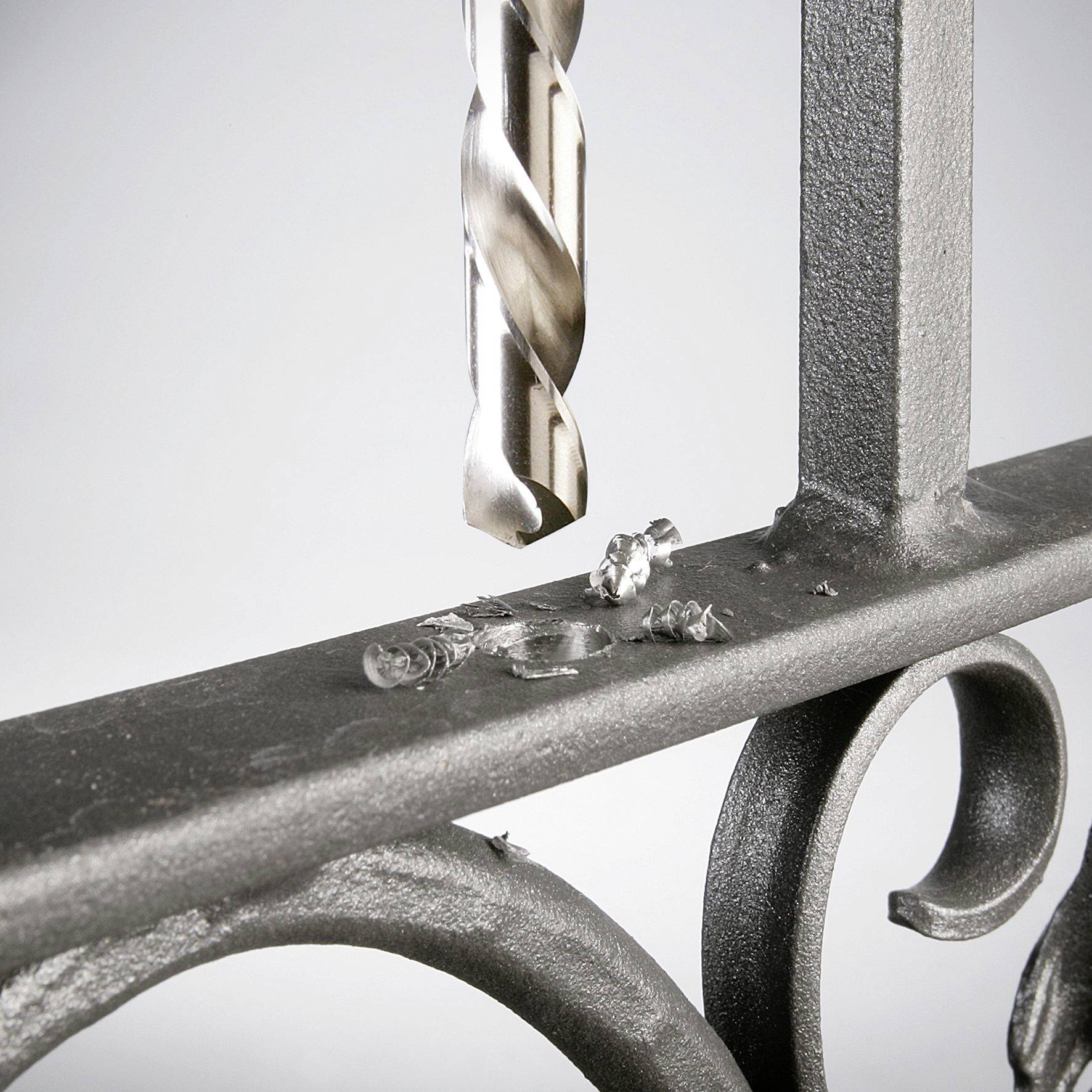 Ein Bohrer durchbohrt Metall, Späne liegen um das Loch. Die Szene zeigt den Arbeitsprozess und die Präzision beim Bohren.