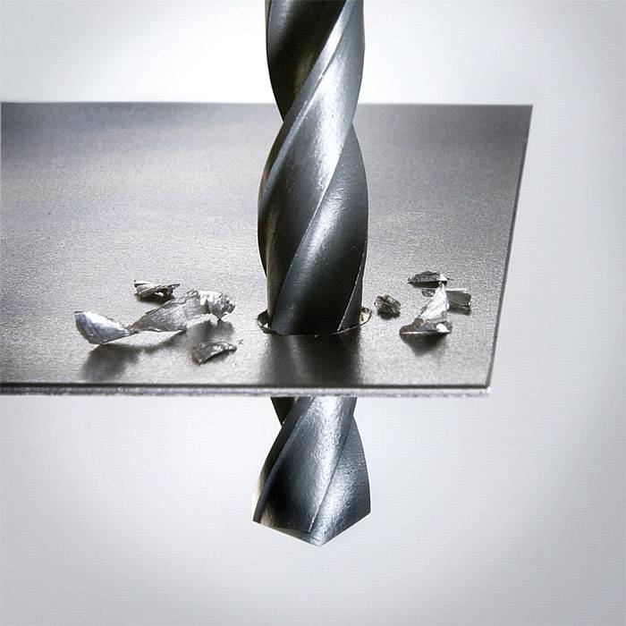 Ein Metallbohrer durchbohrt ein Metallblech, Späne liegen um das Loch herum.