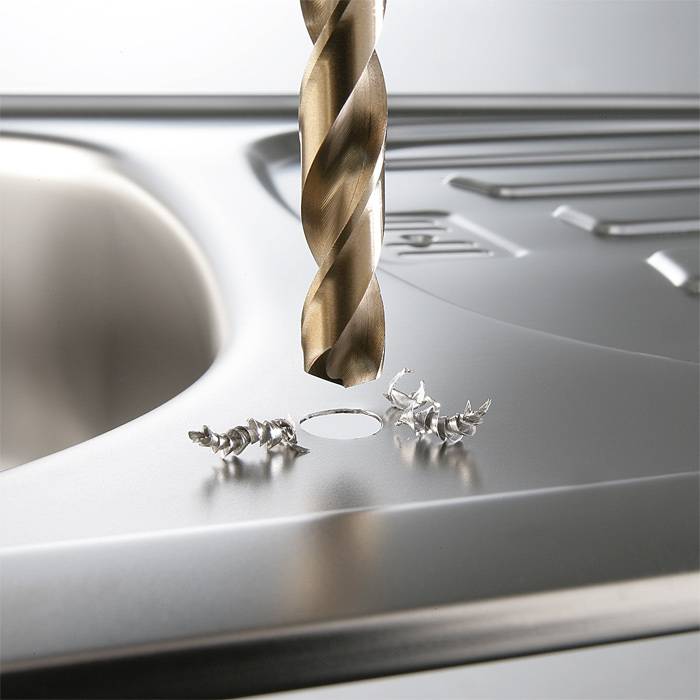 Eine Metallbohrmaschine bohrt ein Loch in eine Edelstahlspüle, umgeben von Metallspänen.