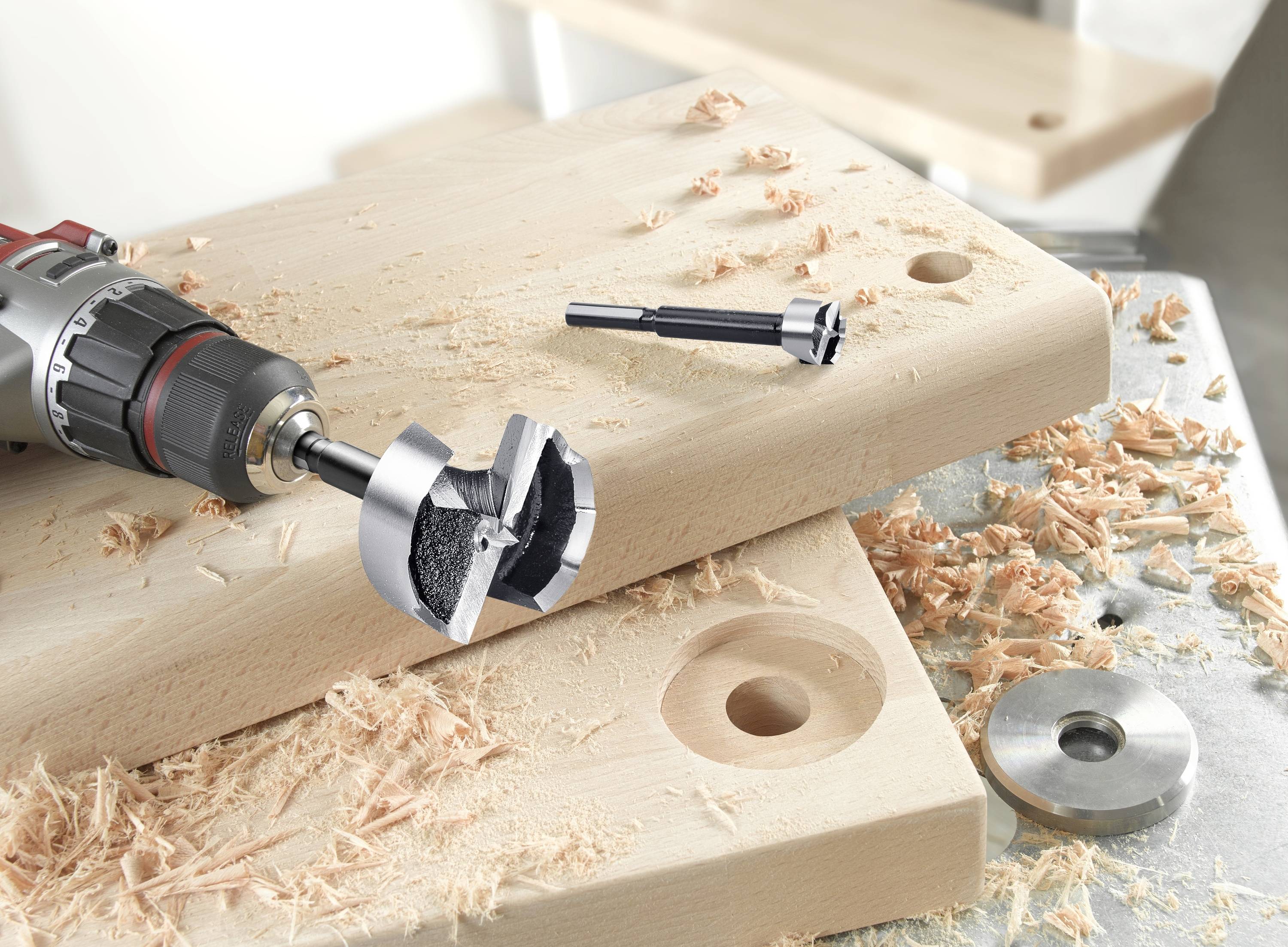 Akkubohrmaschine und Forstnerbohrer bohren präzise Löcher in Holzbrett, umgeben von Holzspänen.